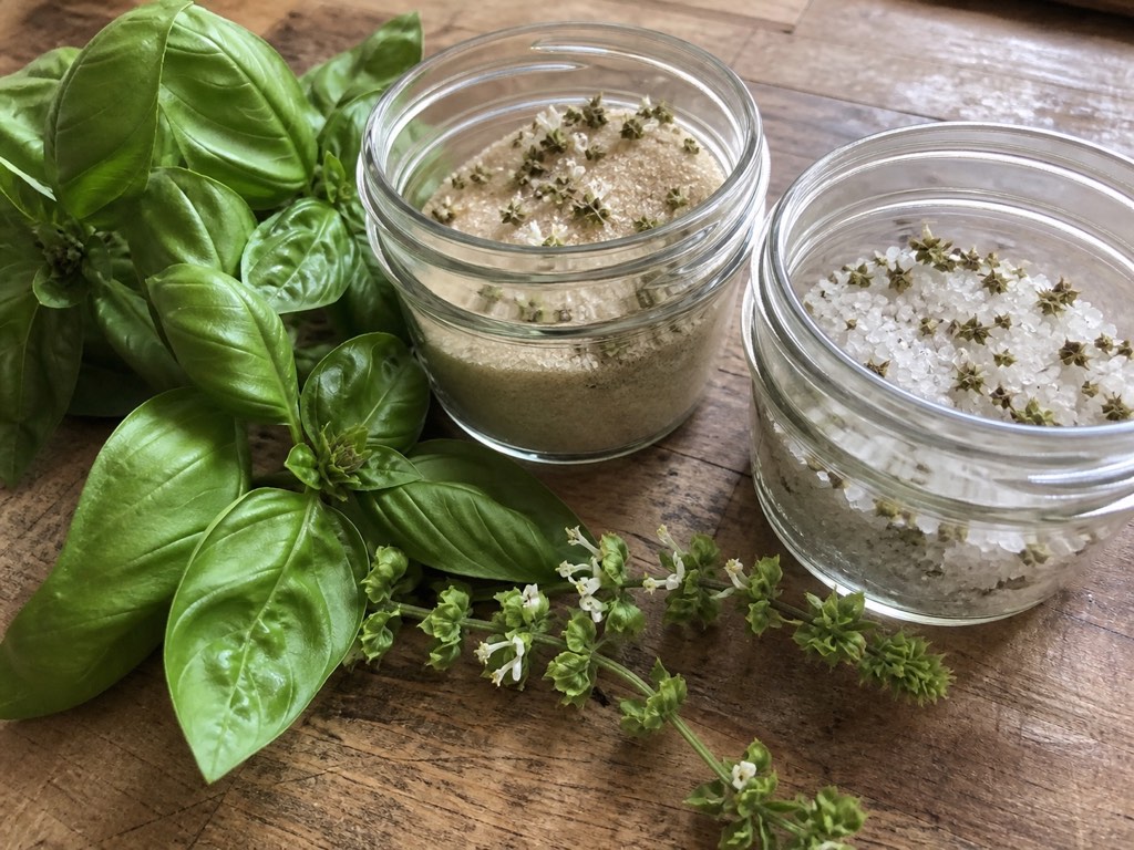 Small jars of basil-flower sugar and salt beside fresh basil leaves and flower spikes